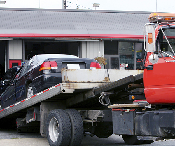 Black vehicle being loaded onto flatbed truck; Agero introduces Tow To Repair
