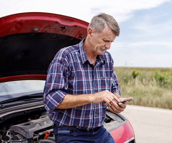 Man stands next to broken down car, uses cell phone