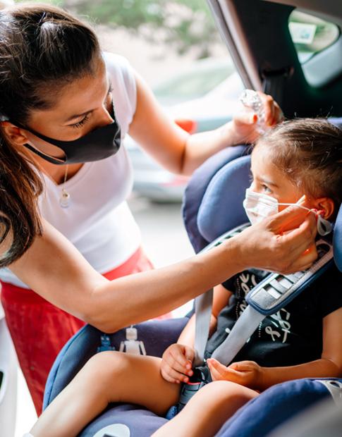 Mom buckling daughter into car seat during COVID - Agero, Inc.